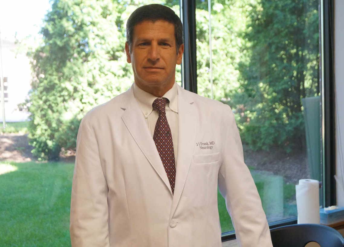 A man in white lab coat and tie standing next to window.